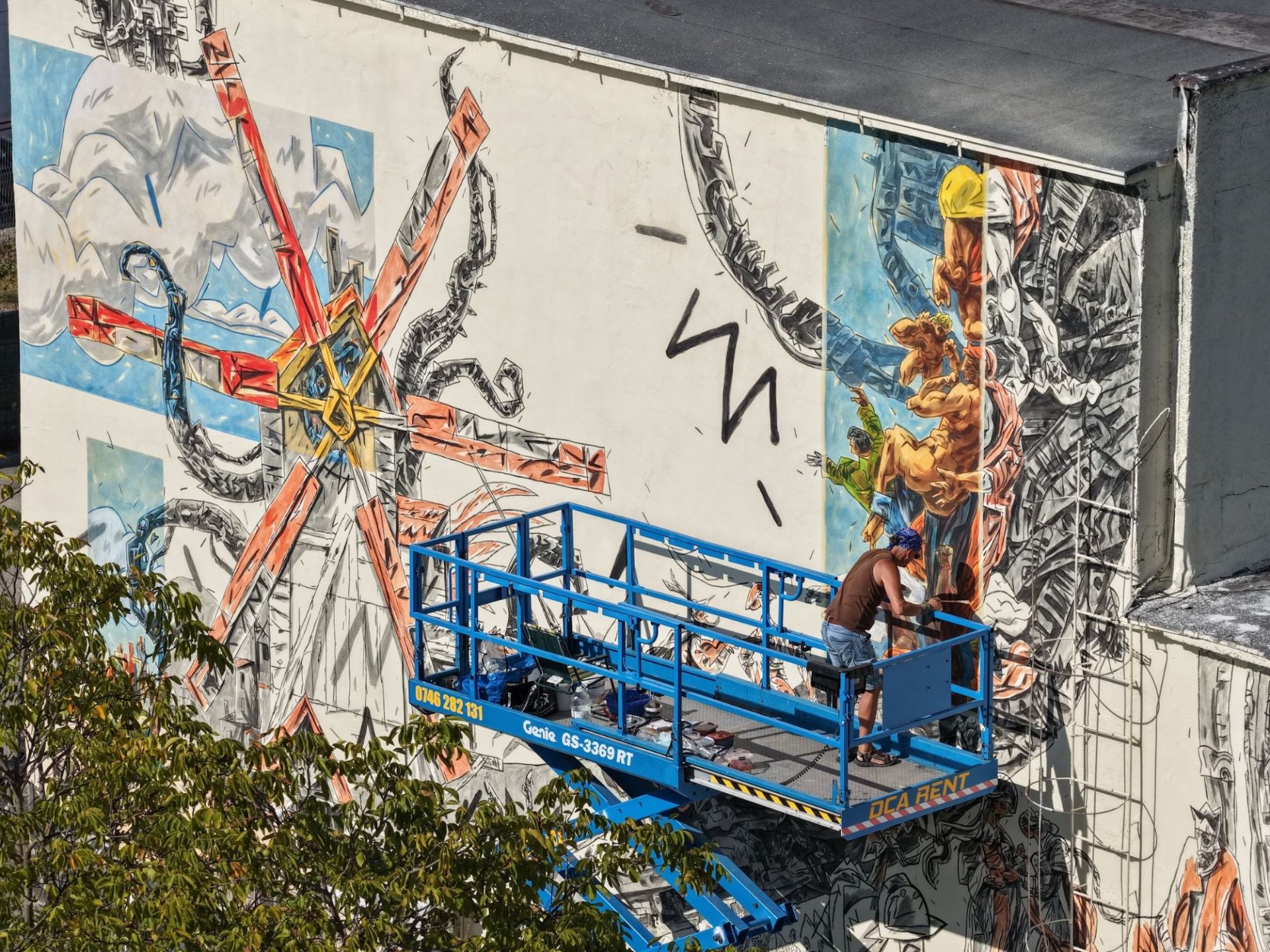The artist painting the Moara Artiștilor mural from a lift platform